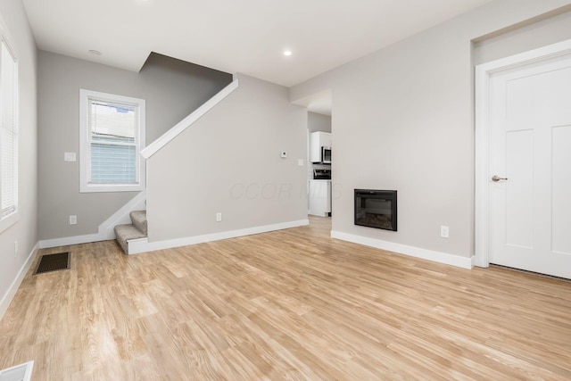 310 S Ogden Ave, Columbus, OH 43204 - unfurnished living room with stairway, light wood-style flooring, a glass covered fireplace, and recessed lighting