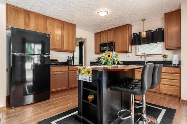 281 Inah Ave, Columbus, OH 43228 - kitchen featuring black appliances, light wood finished floors, brown cabinets, a kitchen bar, and a center island