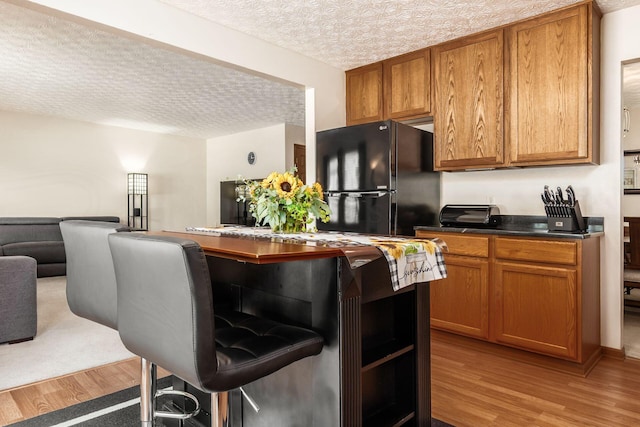 281 Inah Ave, Columbus, OH 43228 - kitchen with freestanding refrigerator, light wood-type flooring, a textured ceiling, brown cabinetry, and dark countertops