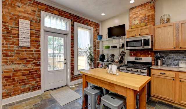 1447 Fair Ave, Columbus, OH 43205 - kitchen featuring appliances with stainless steel finishes, stone tile flooring, brick wall, light brown cabinets, and butcher block counters