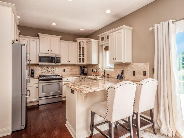 7635 Overland Trl, Delaware, OH 43015 - kitchen featuring stainless steel appliances, a peninsula, glass insert cabinets, a breakfast bar, and light stone counters