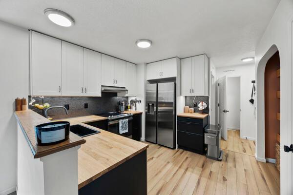 5813 Camhurst Ct, Galloway, OH 43119 - kitchen featuring stainless steel appliances, under cabinet range hood, arched walkways, tasteful backsplash, and white cabinets