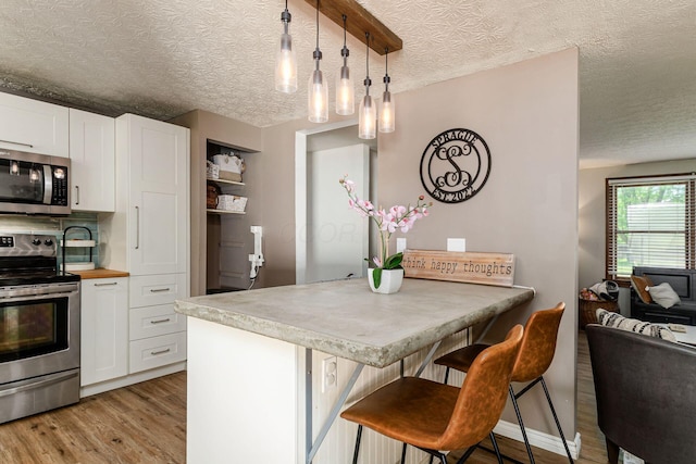 2630 Bella Via Ave, Columbus, OH 43231 - kitchen featuring stainless steel appliances, light wood-type flooring, a textured ceiling, white cabinets, and a kitchen breakfast bar