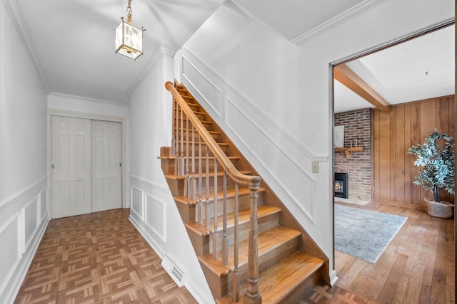 1295 Castleton Rd N, Columbus, OH 43220 - stairway featuring a decorative wall, a brick fireplace, crown molding, wood finished floors, and a wainscoted wall