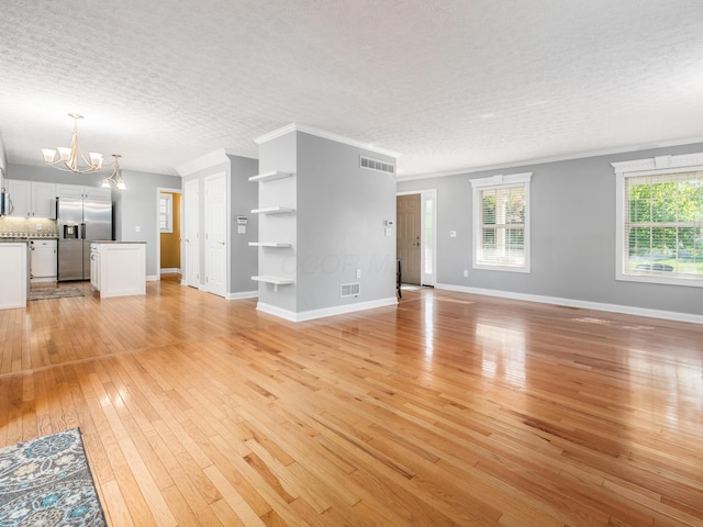 304 Cottage Grove Cir, Pataskala, OH 43062 - unfurnished living room featuring a chandelier, light wood-type flooring, a textured ceiling, and crown molding