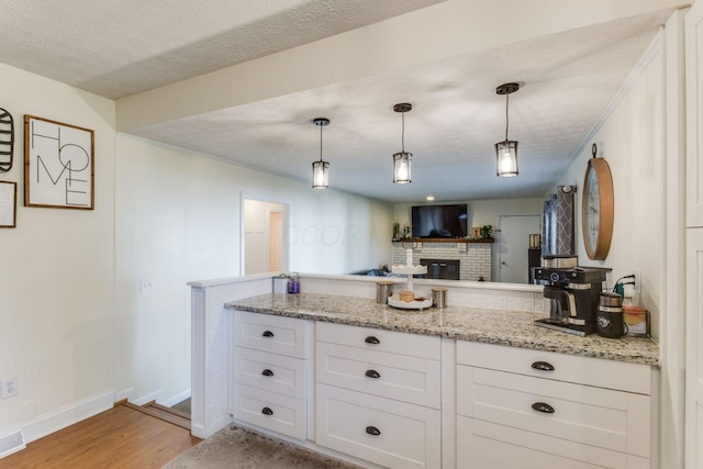 691 Heritage Blvd, Delaware, OH 43015 - kitchen with light wood-style flooring, white cabinets, a brick fireplace, a peninsula, and decorative light fixtures