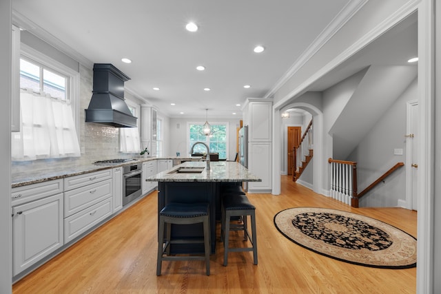 1359 White Oak Ln, New Albany, OH 43054 - kitchen with custom range hood, appliances with stainless steel finishes, ornamental molding, light wood-type flooring, and white cabinetry