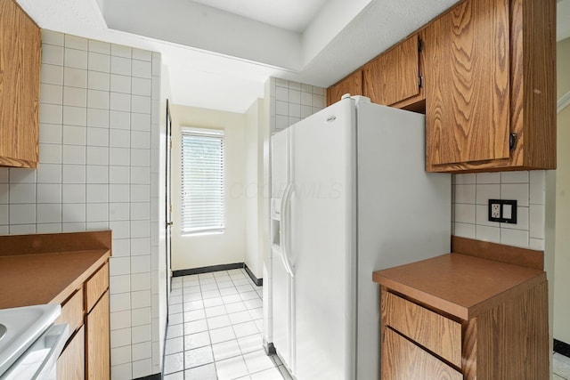 2663 Cedar Lake Dr, Dublin, OH 43016 - kitchen featuring white fridge with ice dispenser, brown cabinetry, light tile patterned floors, backsplash, and stove