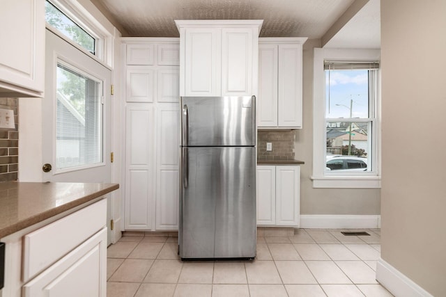 675-677 Beech St, Columbus, OH 43206 - kitchen featuring freestanding refrigerator, backsplash, light tile patterned floors, and white cabinetry