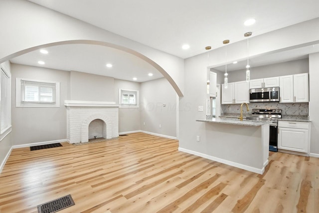 87 N Warren Ave, Columbus, OH 43204 - kitchen featuring stainless steel appliances, arched walkways, light wood-style floors, light stone countertops, and hanging light fixtures