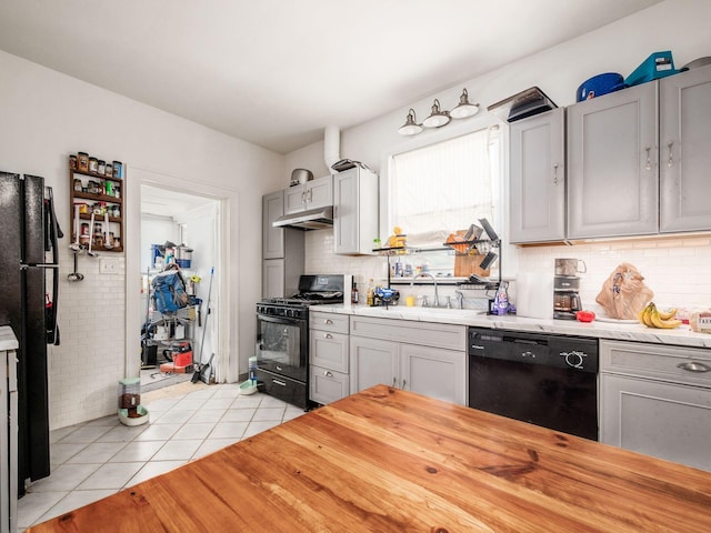 1482 Briarwood Ave, Columbus, OH 43211 - kitchen with black appliances, under cabinet range hood, light tile patterned floors, butcher block countertops, and backsplash