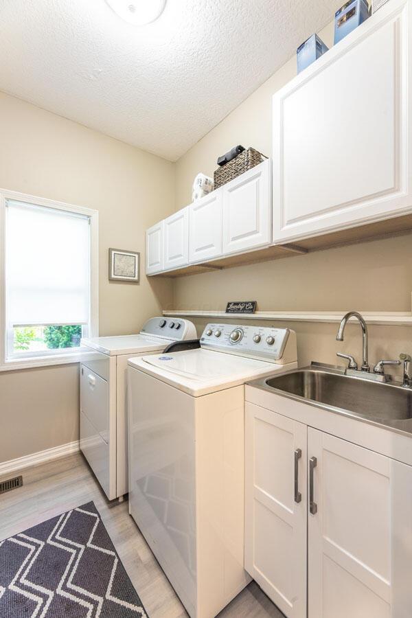 419 Wooten Ct S, Powell, OH 43065 - laundry room with separate washer and dryer, light wood-style floors, cabinet space, and a textured ceiling