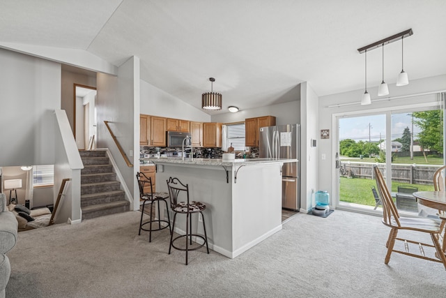 2587 Weeping Willow Ct, Columbus, OH 43207 - kitchen featuring appliances with stainless steel finishes, light carpet, lofted ceiling, brown cabinetry, and a kitchen breakfast bar