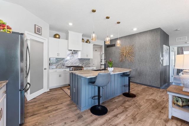 152 Natalie Ln, Granville, OH 43023 - kitchen featuring freestanding refrigerator, wood finished floors, white cabinetry, light stone counters, and an island with sink