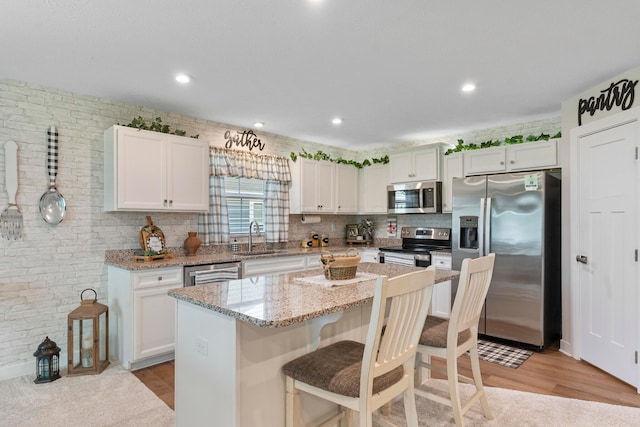 211 Talla Rd S, Delaware, OH 43015 - kitchen featuring stainless steel appliances, a kitchen breakfast bar, white cabinetry, light stone countertops, and light wood-style flooring