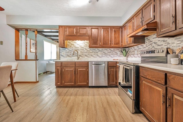 7472 Davis Rd, Hilliard, OH 43026 - kitchen with appliances with stainless steel finishes, under cabinet range hood, light wood-style floors, decorative backsplash, and light countertops