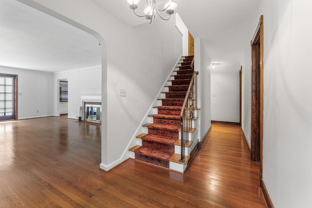 1054 Highland Dr, Columbus, OH 43220 - staircase featuring arched walkways, wood finished floors, a chandelier, and a glass covered fireplace