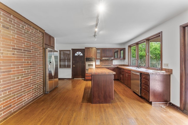 1054 Highland Dr, Columbus, OH 43220 - kitchen featuring appliances with stainless steel finishes, tile counters, a kitchen island, wood finished floors, and glass insert cabinets