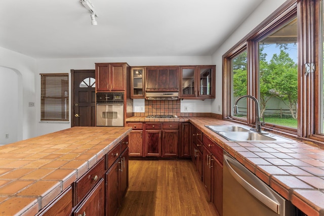 1054 Highland Dr, Columbus, OH 43220 - kitchen featuring appliances with stainless steel finishes, tile countertops, dark wood-style floors, glass insert cabinets, and track lighting