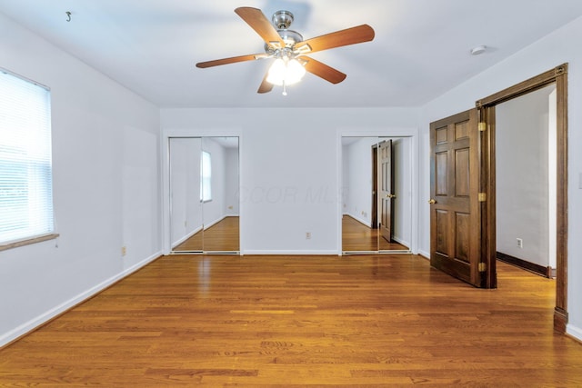 1054 Highland Dr, Columbus, OH 43220 - unfurnished bedroom with two closets, multiple windows, wood finished floors, and a ceiling fan