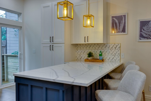 1017 Madison Ave, Columbus, OH 43205 - kitchen with a peninsula, white cabinets, light stone countertops, a breakfast bar area, and decorative light fixtures