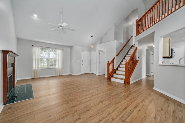 8135 Barlow Rd, Westerville, OH 43081 - unfurnished living room with ceiling fan, high vaulted ceiling, stairway, light wood-style floors, and a tile fireplace