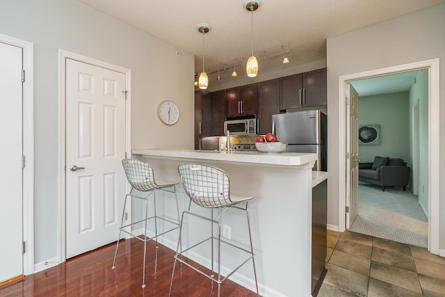 115 E Noble St Unit 2, Columbus, OH 43215 - kitchen featuring appliances with stainless steel finishes, light countertops, a breakfast bar, dark brown cabinetry, and pendant lighting
