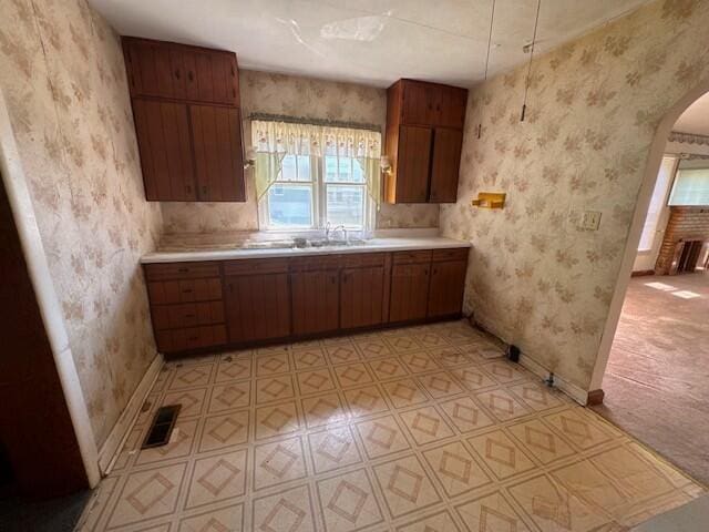 498 E Mark St, Marion, OH 43302 - kitchen featuring arched walkways, wallpapered walls, light countertops, light flooring, and brown cabinets