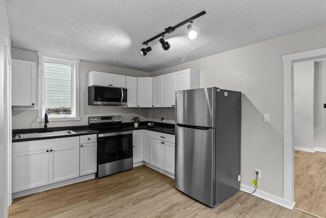 508 E Welch Ave, Columbus, OH 43207 - kitchen with appliances with stainless steel finishes, a textured ceiling, dark countertops, light wood-style flooring, and white cabinetry