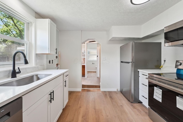 1366 Brown Rd, Columbus, OH 43223 - kitchen featuring appliances with stainless steel finishes, light wood-style flooring, light countertops, white cabinetry, and a textured ceiling