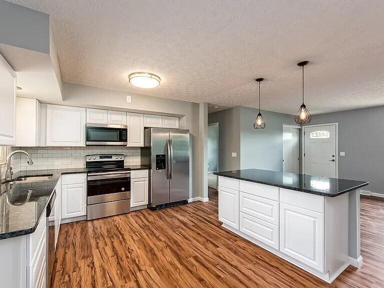 5717 Karl Rd, Columbus, OH 43229 - kitchen featuring stainless steel appliances, dark wood finished floors, backsplash, white cabinetry, and a kitchen island