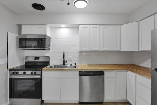 1615 Coronet Dr, Columbus, OH 43224 - kitchen featuring appliances with stainless steel finishes, butcher block counters, decorative backsplash, white cabinets, and a textured ceiling