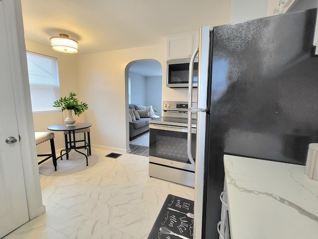 570 N Ohio Ave, Columbus, OH 43203 - kitchen featuring appliances with stainless steel finishes, arched walkways, light marble finish floors, light stone countertops, and white cabinetry