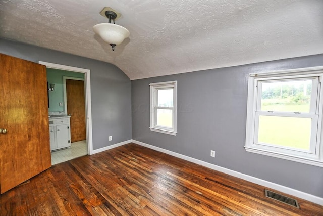 7579 Rangeline Rd, Mount Vernon, OH 43050 - unfurnished bedroom featuring hardwood / wood-style floors, multiple windows, a textured ceiling, vaulted ceiling, and connected bathroom