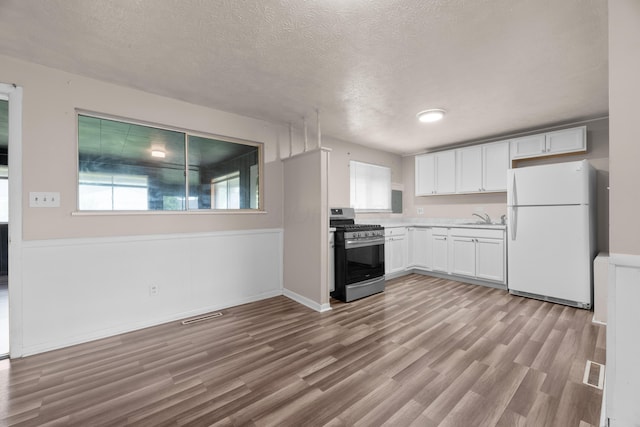 3505 Roswell Dr, Columbus, OH 43227 - kitchen with stainless steel gas stove, freestanding refrigerator, a textured ceiling, white cabinetry, and wood finished floors