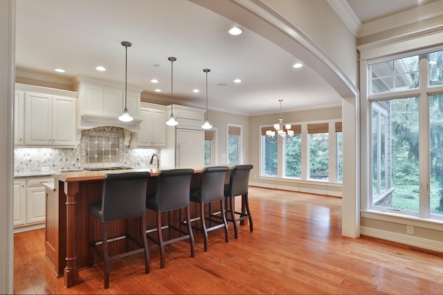 580 Keyes Ln, Worthington, OH 43085 - kitchen featuring light wood-type flooring, crown molding, backsplash, a chandelier, and a kitchen island with sink