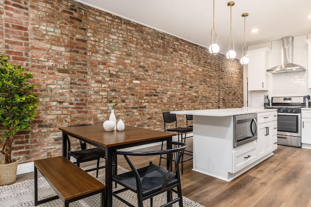 887-891 S 22nd St, Columbus, OH 43206 - kitchen with appliances with stainless steel finishes, wall chimney exhaust hood, brick wall, light countertops, and white cabinets