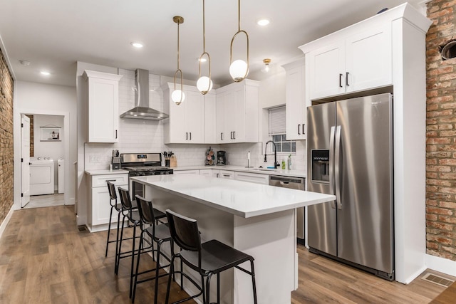 887-891 S 22nd St, Columbus, OH 43206 - kitchen featuring appliances with stainless steel finishes, wall chimney range hood, washer and clothes dryer, dark wood finished floors, and a kitchen breakfast bar