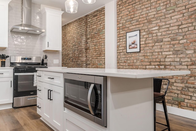 887-891 S 22nd St, Columbus, OH 43206 - kitchen featuring wall chimney range hood, appliances with stainless steel finishes, a kitchen bar, light countertops, and brick wall