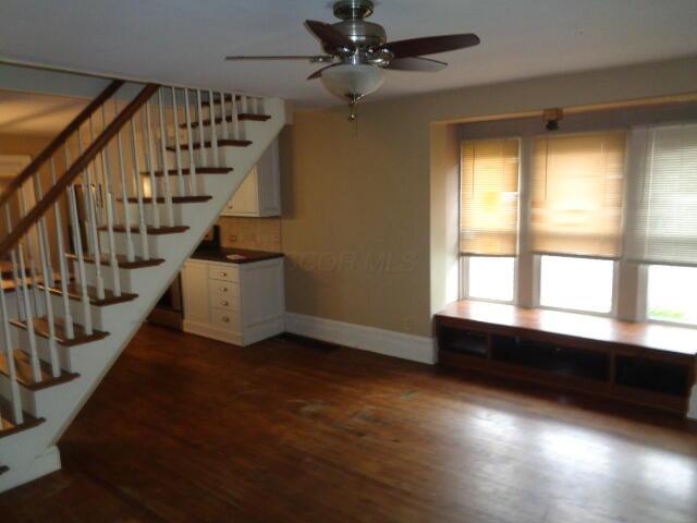 312 W William St, Delaware, OH 43015 - unfurnished living room with stairs, ceiling fan, and dark wood-style flooring