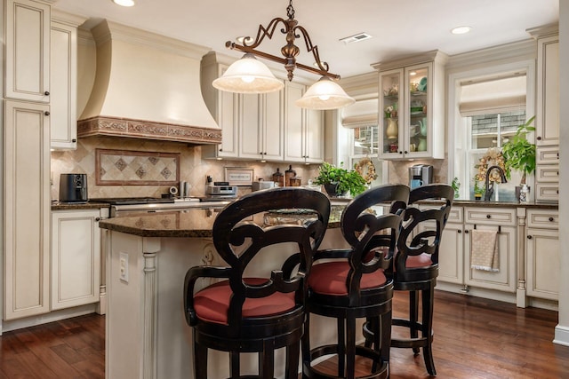 161 Jackson St, Columbus, OH 43206 - kitchen with custom range hood, cream cabinets, a kitchen bar, a center island, and backsplash