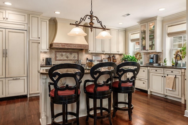 161 Jackson St, Columbus, OH 43206 - kitchen with cream cabinets, dark countertops, paneled built in fridge, a breakfast bar, and glass insert cabinets