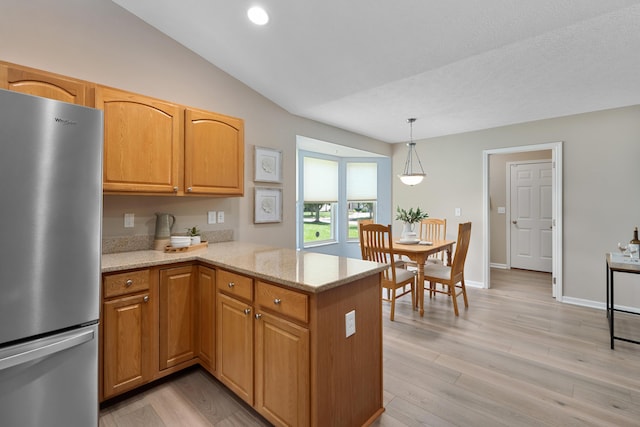 8090 Tree Lake Blvd, Powell, OH 43065 - kitchen featuring freestanding refrigerator, a peninsula, light stone counters, light wood finished floors, and hanging light fixtures