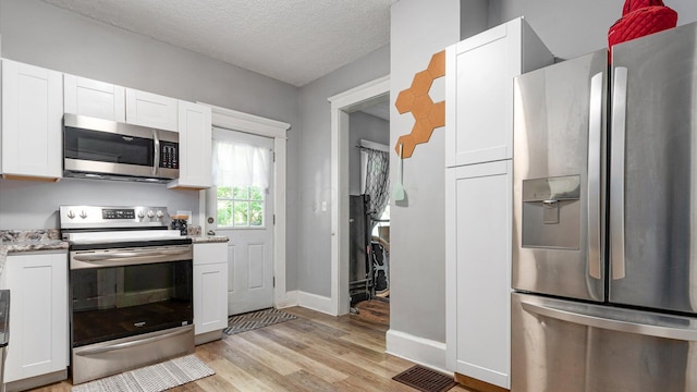 467 Mount Vernon Rd, Newark, OH 43055 - kitchen featuring stainless steel appliances, light wood finished floors, white cabinetry, a textured ceiling, and light stone countertops