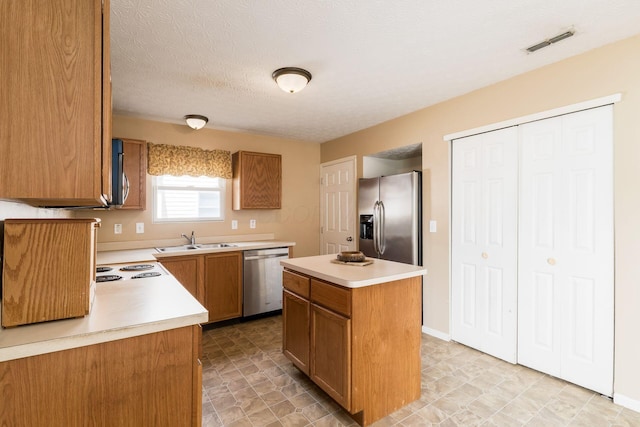 7787 Freesia St Unit 216, Blacklick, OH 43004 - kitchen with appliances with stainless steel finishes, light countertops, a kitchen island, brown cabinetry, and a textured ceiling