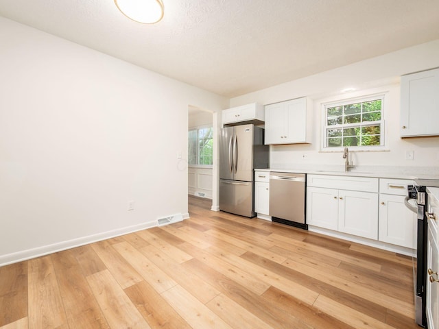 6019 Beechcroft Rd, Columbus, OH 43229 - kitchen with appliances with stainless steel finishes, light countertops, white cabinetry, light wood-style floors, and plenty of natural light