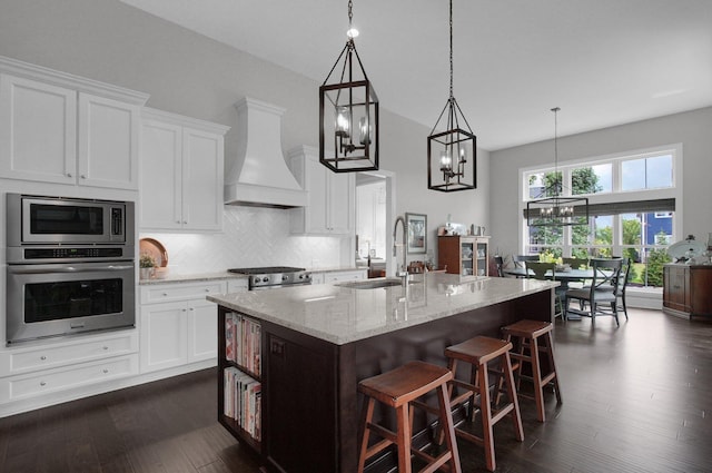 7211 Craigens Ct, Plain City, OH 43064 - kitchen with appliances with stainless steel finishes, custom range hood, a chandelier, an island with sink, and light stone counters