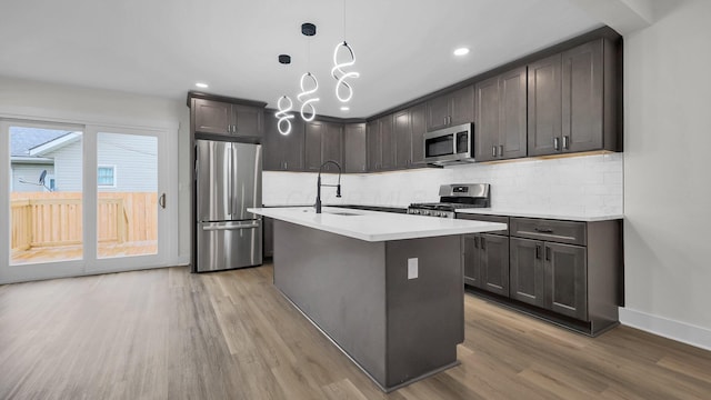 732 Columbus Ave, Washington Court House, OH 43160 - kitchen featuring stainless steel appliances, light wood finished floors, decorative backsplash, light countertops, and an island with sink