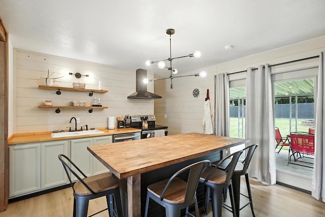3139 Woonsocket St, Springfield, OH 45503 - kitchen with butcher block counters, light wood-style flooring, wall chimney range hood, appliances with stainless steel finishes, and wooden walls