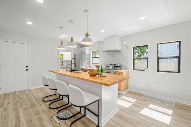 628 E Gates St, Columbus, OH 43206 - kitchen featuring premium range hood, appliances with stainless steel finishes, butcher block counters, light wood-style flooring, and a breakfast bar area